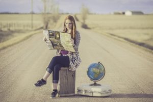 Woman sitting on suitcase to represent journey.