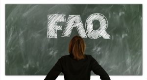 Woman looking at the letters "FAQ" (frequently asked questions) written on a chalkboard.