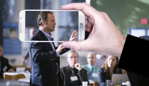 Man speaking in public and person taking a photo of them to illustrate thought leadership.